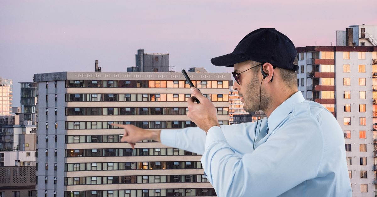 Security guard holding walkie talkie pointing against buildings